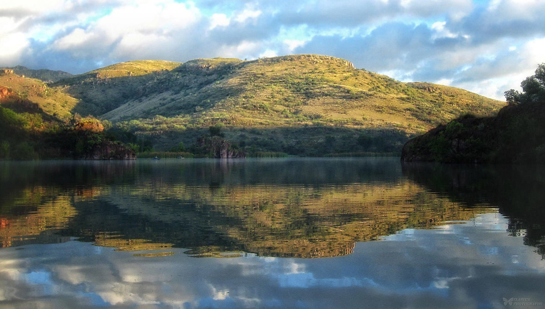 A reflection of the illuminated  hillside in the calm, still waters of Pena Blanca Lake.